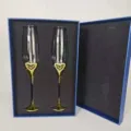 Nahaufnahme eleganter Kristall-Champagnergläser mit Herzmotiven in blauer Geschenkbox - 2 Goldene Becher Packung / Geschenkbox