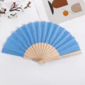 Ventaglio pieghevole blu con stecche in legno naturale, superficie in tessuto, mano. - Celeste