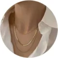Detailed view of triple-layered gold chain necklaces on a white shirt background - Three-layer Mixed Chain (Double Snake+Wide)