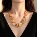 Vista dettagliata della collana in madreperla dorata su modella con top nero con scollo a V - Caffè