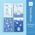 Vista dettagliata di quattro quaderni a spirale A5 con simpatici squali blu cartoon. - Album dello Squalo