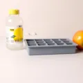 Side view of a fifteen-compartment gray silicone ice cube tray placed on a plain white surface - With Cover / Blue