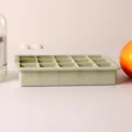 Side view of a 15-grid sage green silicone ice cube tray on a clean white table. - With Cover / Green