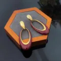 Close-up shot of elegant burgundy red and gold oval drop earrings on a wooden display stand - Geometric Oval Style (E3625 Wine Red) / Wine Red (E3625 Wine Red)