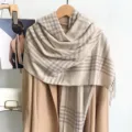 Détail d'une écharpe à carreaux beige à pompons drapée élégamment sur un manteau d'hiver beige - Z256 / Beige