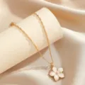 Dettaglio macro di un'elegante collana con ciondolo a fiore dorato su seta champagne - Bianco
