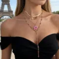 Primo piano di una collana dorata a strati con pendente a fiore rosa davanti alla Torre Eiffel a Parigi - Stile Petalo Rosa / Oro + Rosa