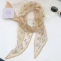 Primer plano de un elegante pañuelo de gasa floral con accesorios de estilo minimalista - Encaje Caqui