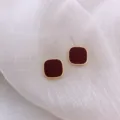 Detailed macro view of minimalist square stud earrings with dark red finish and gold border. - Square Rounded Corner Style (E0131)