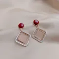 Close-up of elegant gold-toned square drop earrings with red studs and sparkling crystals - Geometric Square Color-Block Style (E0421)