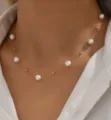 Close-up van een delicate gouden ketting met witte parels om de nek van een model. - Goud