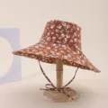 Detailed view of a brown floral print wide-brim sun hat on a wooden display stand. - Adult 55-58cm / Brown with White Floral (5)