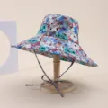 Detailed view of a wide-brimmed floral sun hat with a chin strap on a wooden stand - Adult 55-58cm / Vivid Floral Print (11)