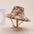 Detail view of a floral wide-brim sun hat with chin strap on a wooden stand for sun protection. - Adult 55-58cm / Red and Yellow Floral Print (12)