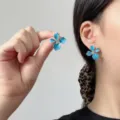 Detail der blauen Emaille-Blumenohrstecker zeigt Tragekomfort und Handvergleich - Emaillierte Blume Strass Ohrstecker (E5355) / Blau und Weiß Kontrast