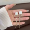 Macro detail of white rose earrings with rhinestone bows and long golden tassels. - Rose Bow Tassel Style (E3626) / Gold (E3626)
