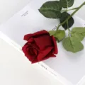 Deep red artificial rose with moisturizing texture lying on a white book surface - Red