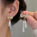 Elegant sparkling bow stud earrings with dangling crystal tassels shown on ear and hand - Pavé Rhinestone Bowknot Tassel Stud Earrings (E2628金)