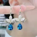 Elegant gold-tone floral earrings featuring white petals and blue pear-shaped crystal pendants. - Dark Blue Water Drop Floral Earrings (E2561 Blue)