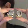 Close-up of irregular textured oval silver and gold earrings held by model - Lava Texture Oval Style (E4377) / Gold and Silver