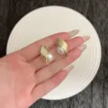 Élégantes boucles d'oreilles en métal doré brossé avec grandes perles blanches sur main. - Boucles d'Oreilles Clous Perle Enveloppée en Métal Brossé (E5018) / Or