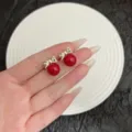 Vintage style earrings featuring vibrant red pearls and delicate gold bowknots displayed on hand - Bowknot Red Bead Stud Earrings (E4250) / Red