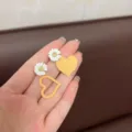 Asymmetric yellow heart and white daisy stud earrings displayed on a palm for scale. - Daisy Orange Heart Style (E2774 Orange)