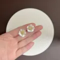 Nahaufnahme eleganter weißer Kamelien-Ohrstecker mit gelber Strass-Mitte in der Hand. - Kamelie Strass Ohrstecker (E5356) / Gold