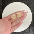 Detailansicht cremefarbener 3D-Blumen-Ohrstecker in der Hand mit zarten Blütenblättern - Gelb (E5044) / Gelb