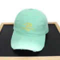 Close-up detail of mint green distressed baseball cap featuring yellow letter embroidery - Adult 56-60cm / Green