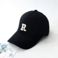 Détail d'une casquette de baseball noire avec un écusson brodé blanc en forme de lettre R - Adulte 55-59cm / Noir