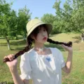 Close-up of a minimalist light green bucket hat worn by a model in an outdoor park. - Adult 56-58cm / Bucket Hat Style / Fresh Green