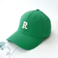 Close-up of a green baseball cap featuring a white embroidered letter R on the front - Adult 55-59cm / Green