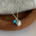 Primo piano di una collana con ciondolo a tazza argentata con una perla blu turchese - Girocollo con Ciondolo a Forma di Tazza (R5688)