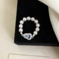 Primo piano di un elegante anello elastico di perle con un ciondolo a cuore in zircone blu. - R0670 Anello Elastico Zucca Blu Mare Chiaro / Azzurro