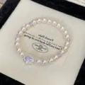 Vista dettagliata di un elegante bracciale di perle con cristalli viola e pietra centrale. - Stile Gemma Ovale (R1688) / Viola