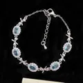 Elegante pulsera plateada con circonitas ovaladas azul claro y dijes de lazo de diseño único - Estilo de Lazo Azul Cielo (R1841)