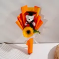 Nahaufnahme des Abschluss-Sonnenblumen- und Bären-Blumenstraußes in orangefarbenem Papier. - Orange