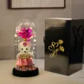 Gedetailleerd overzicht van een LED glazen koepel met roze roos en beer voor cadeau. - Zwarte golfkartonnen doos, beer & roze bloemen