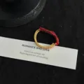 Close-up of C-shaped metallic ring with red seed beads on a textured black background. - Size 6