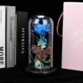 Vue détaillée de la rose éternelle sous dôme en verre avec fleur bleue, papillon et lumières LED. - Télécommande USB fleur violette à bord doré trèfle avec papillon évidé (Base noire)