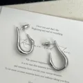 Close-up van minimalistische onregelmatige U-vormige zilveren oorknopjes - Zilver