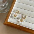 Elegant gold-toned hoop earrings with white pearl flower pendants shown in close-up view - Flower Drop Earrings