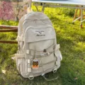 Beige minimalist large capacity student backpack displayed on green grass in sunlight - With Pendant / Off White