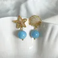 Asymmetrische, vergoldete Seestern- und Muschelohrringe mit hellblauen Natursteinperlen verziert. - Asymmetrischer Seestern Muschel (Blaue Perle) / Gold/Blau