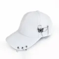 Close-up detail of a white baseball cap featuring metal rings on the brim and a butterfly chain pin. - White Butterfly Pin
