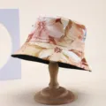 Close-up view of a floral print bucket hat on a wooden stand for vacation sun protection - Orange Brown Floral Print