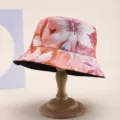 Close-up of reversible bucket hat with elegant pink floral print on wooden stand - Orange Pink