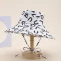 Close-up of wide-brim bucket hat with artistic brush-stroke letter print and chin drawstring. - English Alphabet White