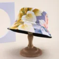 Detailed view of a reversible summer floral print bucket hat displayed on a wooden hat stand. - 黄白粉大花卉印花